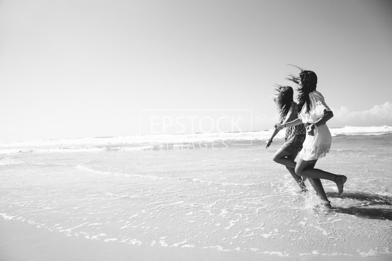 two sisters running on beach holding hands